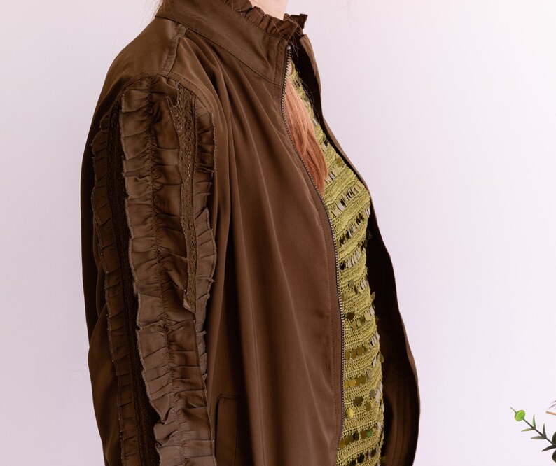 May include: A brown bomber jacket with a zipper closure and ruffled detailing on the sleeves.