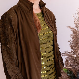 May include: A brown bomber jacket with a zipper closure and ruched sleeves. The jacket is worn over a green sequined top.