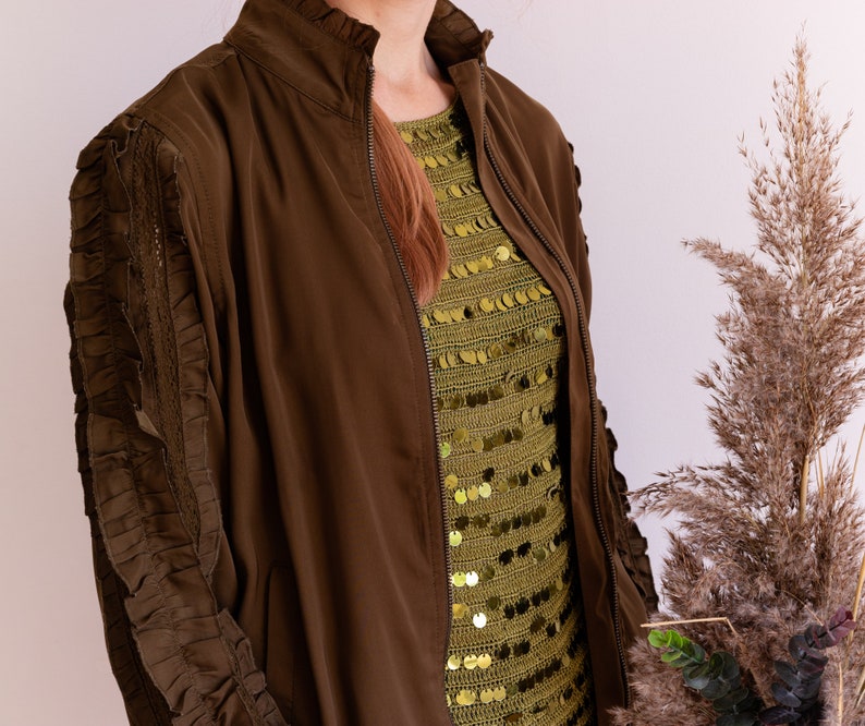 May include: A brown bomber jacket with a zipper closure and ruched sleeves. The jacket is worn over a green sequined top.