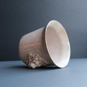 May include: A white ceramic planter with a sculpted animal face on the side. The planter is tilted to the side, revealing the interior.