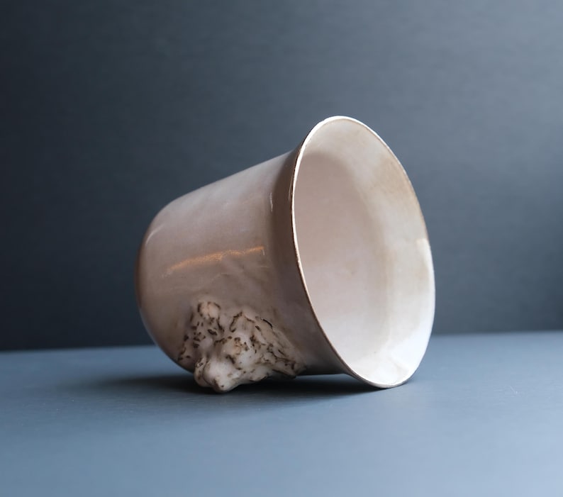 May include: A white ceramic planter with a sculpted animal face on the side. The planter is tilted to the side, revealing the interior.