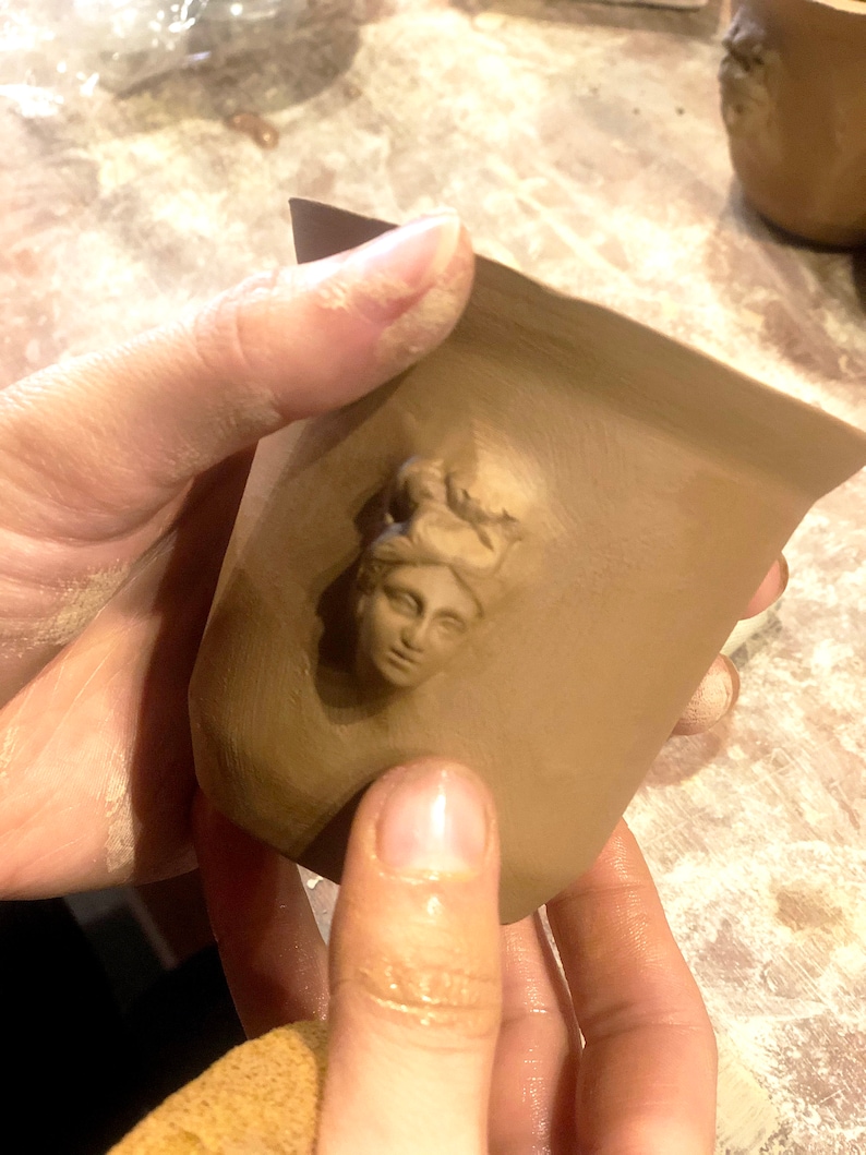 May include: A brown ceramic mug with a raised image of a woman's face on the front.