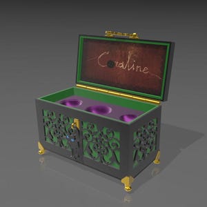 May include: A decorative black chest with green and gold accents, featuring intricate cut-out designs. The interior is green with three purple cup holders. The lid is open, revealing the name "Coraline" in script. The chest has gold feet.