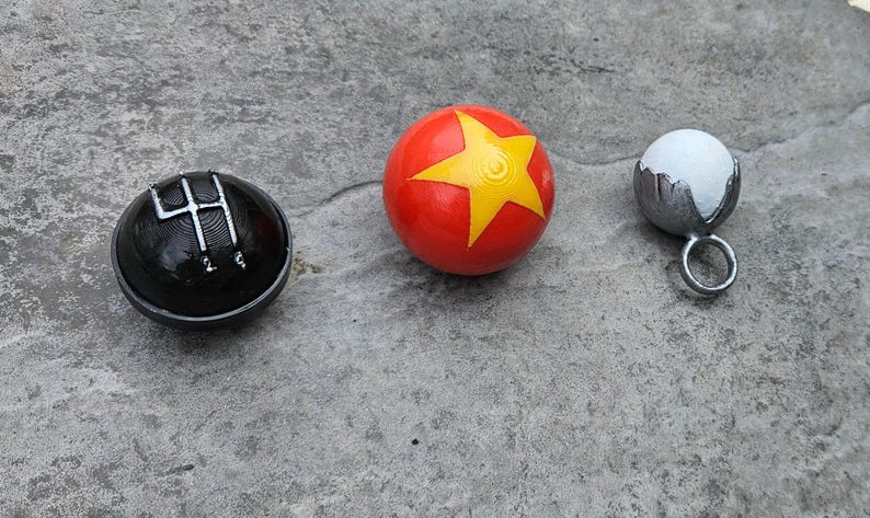 May include: Three spherical objects: a black shift knob with a silver gear pattern, a red ball with a yellow star, and a small white ball in a silver holder with a ring.