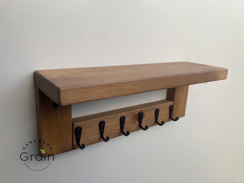 May include: A wooden shelf with six black metal hooks, labeled "Handmade Grain".