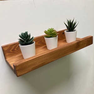 May include: A wooden shelf with three small white pots containing green succulents. The shelf is stained a dark brown color.