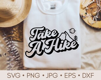 Może przedstawiać: Biały t-shirt z czarnym nadrukiem, na którym widnieje napis "Take A Hike" w retro czcionce. Nadruk zawiera również górę, słońce i sosnę.