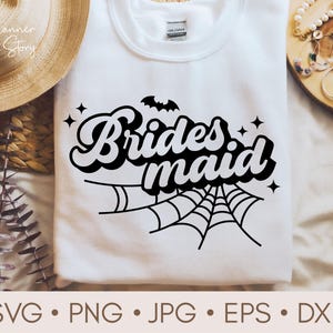 Könnte beinhalten: Weißes T-Shirt mit schwarzem Text, der "Bridesmaid" in einer Retro-Schriftart mit einem Spinnennetz- und Fledermaus-Motiv sagt.