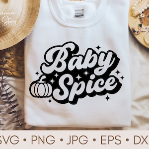 Pode incluir: Camiseta branca com texto preto que diz "Baby Spice" em uma fonte retrô. Uma pequena abóbora preta está à esquerda do texto.