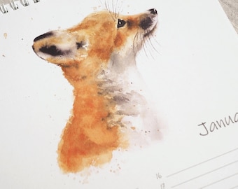 May include: A spiral-bound wall calendar page featuring a watercolour illustration of a fox looking upwards. The fox is rendered in shades of orange, brown, and grey. The text "Janua" is printed on the right side above a list of numbered dates.