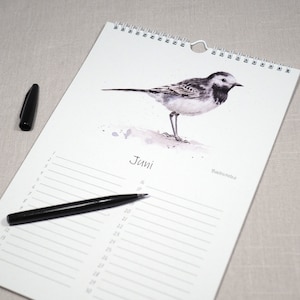 May include: A white calendar with a black and white illustration of a bird on the top. The calendar is for the month of June and has a black pen on it.