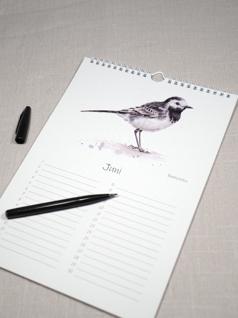 May include: A white calendar with a black and white illustration of a bird on the top. The calendar is for the month of June and has a black pen on it.