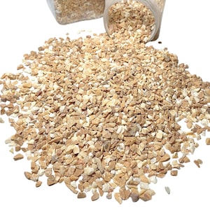 May include: A close-up of a pile of small, light brown and white crushed stones. The stones are scattered on a white background.