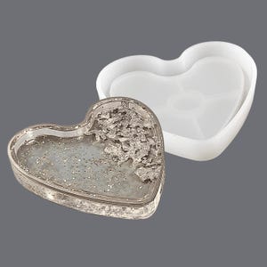 May include: A heart-shaped silicone mould for resin casting. The mould is open and shows a finished resin casting with silver glitter and flakes.