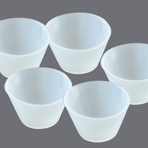 May include: Five white silicone cups, all the same size and shape, are arranged in a circle on a grey background.