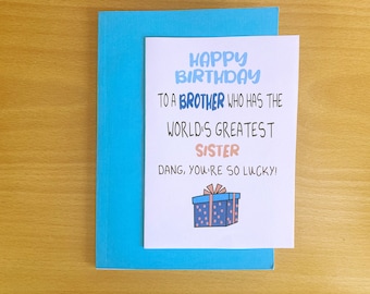 May include: A white card with blue and pink text that reads "Happy Birthday to a brother who has the world's greatest sister. Dang, you're so lucky!"  A cartoon drawing of a blue and pink polka dot gift box with a pink ribbon is at the bottom of the card.