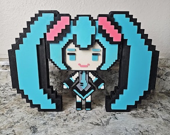 May include: A pixelated figurine of a character with light blue pigtails, pink accents, and a black and white outfit. The figure is surrounded by a pixelated frame in matching colors. The design is reminiscent of retro video game graphics.