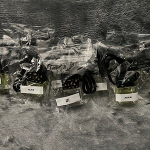 K&ouml;nnte beinhalten: Mehrere kleine Glasflaschen mit schwarzen Deckeln und schwarzen Schn&uuml;ren sind in durchsichtigen Plastikt&uuml;ten verpackt. Die Flaschen sind mit einer klaren Fl&uuml;ssigkeit gef&uuml;llt und tragen Etiketten mit der Aufschrift "Alien" und "CK 001". Der Text "Autodiffusoren, die gestern hergestellt wurden" ist oben im Bild sichtbar.