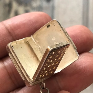 Op de afbeelding: Een zilveren en gouden medaillon met een scharnierend deksel en een ketting. Het medaillon is versierd met een gegraveerd bloemenpatroon.