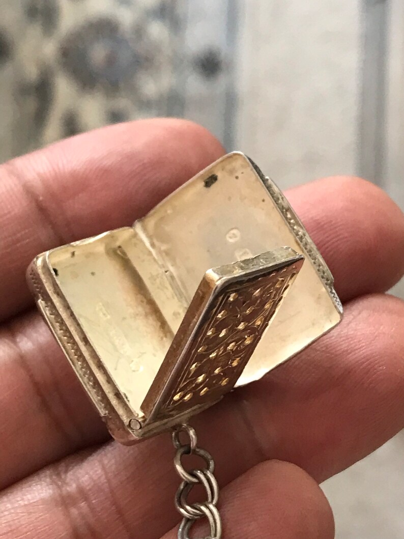 Op de afbeelding: Een zilveren en gouden medaillon met een scharnierend deksel en een ketting. Het medaillon is versierd met een gegraveerd bloemenpatroon.