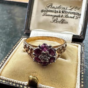 May include: A gold ring with a floral design, set with deep red gemstones and a central diamond, presented in a vintage jewellery box. The box displays the text "Prestons Ltd Goldsmiths & Silversmiths" in a classic font.