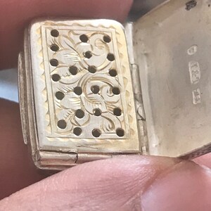 Op de afbeelding: Een zilveren en gouden doos met scharnier, een decoratief bloemenpatroon en gaten. De doos is open en de binnenkant is goud. De doos heeft de inscriptie "837" aan de buitenkant.