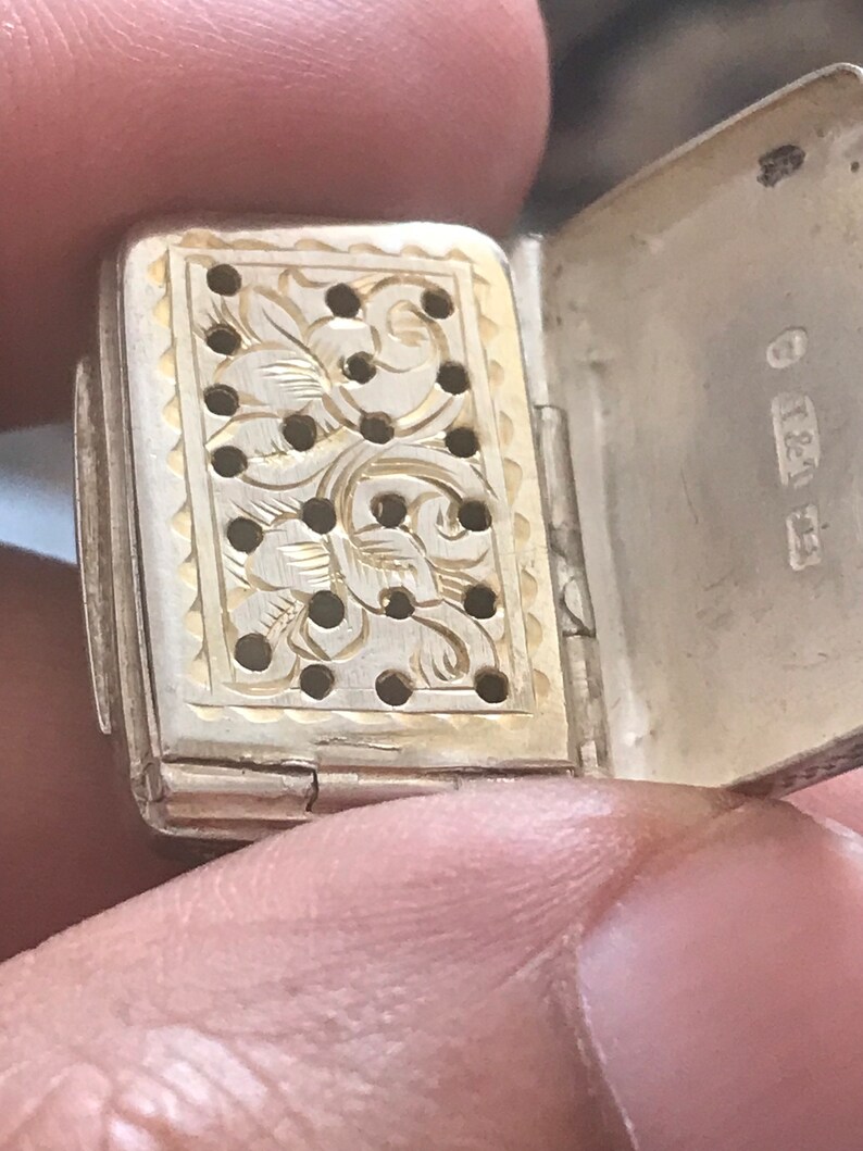 Op de afbeelding: Een zilveren en gouden doos met scharnier, een decoratief bloemenpatroon en gaten. De doos is open en de binnenkant is goud. De doos heeft de inscriptie "837" aan de buitenkant.
