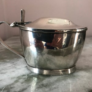 Puede incluir: Un azucarero de plata con tapa abatible y asa. El cuenco es redondo y tiene una superficie lisa y pulida.