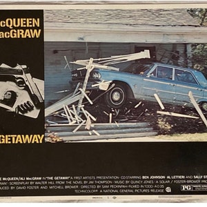 以下が含まれることがあります： スティーブ・マックイーンとアリ・マッグローが出演する映画「ザ・ゲッタウェイ」のポスター。明るい青色の車が木造の構造物に衝突している様子が描かれています。左側にはタイトル、俳優名、銃、俳優の画像が配置されています。
