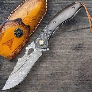 May include: A custom-made knife with a patterned blade and a dark wooden handle. The knife features ornate metalwork and is accompanied by a brown leather sheath with decorative accents. A leather cord is attached to the handle.