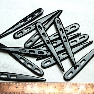 Puede incluir: Un montón de agujas de crochet de plástico negro con una regla en la parte inferior de la imagen. Las agujas tienen un extremo puntiagudo y un bucle en el otro extremo.