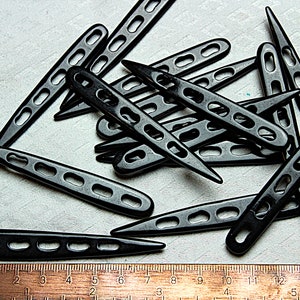 Puede incluir: Un montón de agujas de crochet de plástico negro con una regla en la parte inferior de la imagen. La regla está marcada en pulgadas.