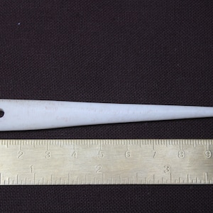 Puede incluir: Un enhebrador de aguja de plástico blanco con un bucle en un extremo y una punta puntiaguda en el otro. El enhebrador mide aproximadamente 10 cm de largo.