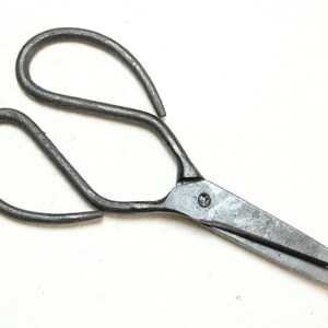 Puede incluir: Un par de tijeras de metal antiguas con un diseño sencillo. Las tijeras tienen un solo remache que conecta las cuchillas y los mangos.