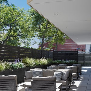 May include: A patio with a black wooden fence, green plants, and gray patio furniture. The furniture is arranged in a seating area with cushions and pillows.
