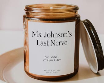 May include: An amber glass jar candle with a white label featuring the black text Ms. Johnson's Last Nerve, Oh look... it's on fire!, and Breathe in the Light 8 oz soy candle. The candle has a black metal lid resting beside it.