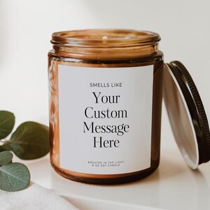 May include: A brown glass jar candle with a white label featuring the black text: SMELLS LIKE Your Custom Message Here BREATHE IN THE LIGHT 8 OZ SOY CANDLE. The candle has a black metal lid resting beside it on a white surface.