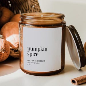 May include: A brown glass jar candle with a white label featuring the text pumpkin spice, BREATHE IN THE LIGHT, SOY WAX CANDLE, and 8 OZ. The candle has a black metal lid placed to the side, and the jar contains a soy wax blend with a visible wick.