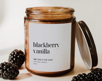 May include: A brown glass jar soy wax candle with a white label featuring the text blackberry vanilla and breathe in the light soy wax candle 8 oz. The candle has a black lid placed to the side, surrounded by several fresh dark blackberries.