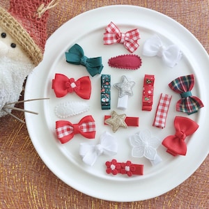 Könnte beinhalten: Eine Auswahl an Haaraccessoires im Weihnachts-Design, darunter Schleifen und Spangen, in Rot, Weiß und Grün. Die Kollektion zeigt verschiedene Muster wie Vichy und Tartan und wird auf einem weißen Teller präsentiert.