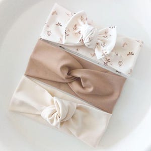 Peut inclure: Trois bandeaux en tissu de différentes couleurs et motifs. Un bandeau est de couleur marron clair, un autre est de couleur beige clair et le troisième est un bandeau blanc avec un motif floral marron.