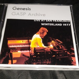 May include: A CD case with a white background and black text that reads "Genesis GASP Archive Live at San Francisco Winterland 1977". The image shows a man playing a keyboard in a dimly lit room.
