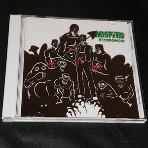 May include: A black and white CD cover with a band called "Misfits" and the album title "Necronomicon". The cover art features a group of figures in black silhouettes with red accents, standing in front of a white splatter.