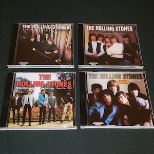 May include: Four compact disc cases with black spines and clear plastic fronts. Each case features a different image of the Rolling Stones band members. The text on the cases reads "The Rolling Stones Remastered Edition" and "Black Box CD 1", "Black Box CD 3", "Special Millennium Edition", and "Remastered Edition".