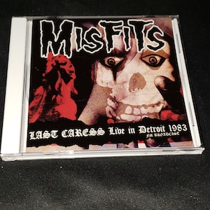 May include: A CD case with a black and white image of a skull with a black and white background. The text "Misfits Last Caress Live in Detroit 1983 FM Broadcast" is printed on the front of the case.