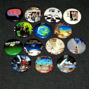 May include: A collection of 12 round button pins featuring album covers from the band Yes. The pins feature various album covers, including "Close to the Edge", "Fragile", "The Yes Album", "Going for the One", "Relayer", "Drama", "90125", "Talk", "Union", "The Ladder", "Open Your Eyes", and "Magnification".