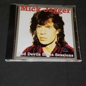 May include: A CD case featuring a close-up photo of Mick Jagger, the lead singer of the Rolling Stones. The case is titled "Red Devils Blues Sessions" and features a black cat logo.