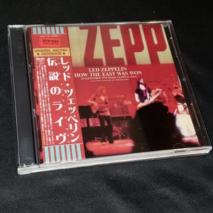 May include: A CD case with a red, white, and blue background. The front of the case features a photo of a band performing on stage. The text "LED ZEPPELIN HOW THE EAST WAS WON 29 SEPTEMBER 1971 OSAKA FESTIVAL HALL LEGENDARY ALT. SOUNDBOARD TAPES" is printed on the case.