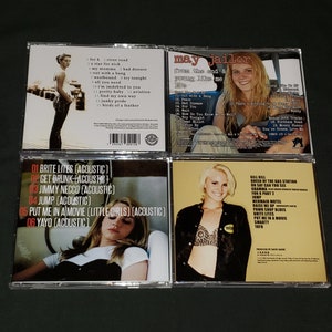 May include: Four compact discs with different album covers. The top left CD features a woman in a black dress standing on a pier. The top right CD features a woman in a car with the text "May Jailer from the end & young like me" on the cover. The bottom left CD features a woman lying down in a car with the text "Brite Lites (Acoustic)" on the cover. The bottom right CD features a woman wearing a black top and a bra with the text "Kill Kill Queen of the Gas Station" on the cover.