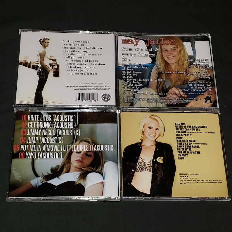 May include: Four compact discs with different album covers. The top left CD features a woman in a black dress standing on a pier. The top right CD features a woman in a car with the text "May Jailer from the end & young like me" on the cover. The bottom left CD features a woman lying down in a car with the text "Brite Lites (Acoustic)" on the cover. The bottom right CD features a woman wearing a black top and a bra with the text "Kill Kill Queen of the Gas Station" on the cover.